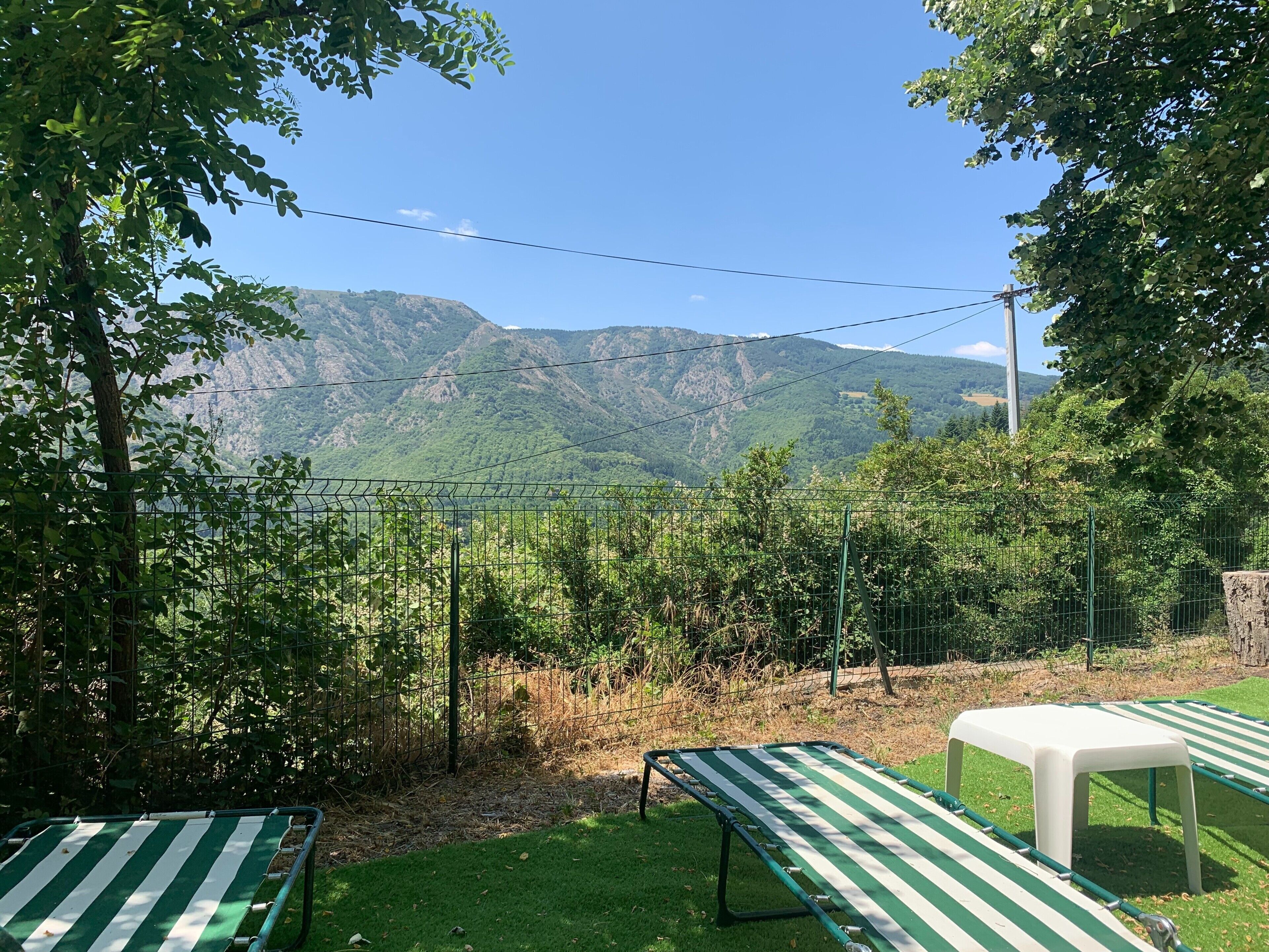 Une zone herbeuse, délimitée par une clôture métallique, avec un banc et une vue sur une chaîne de montagnes.