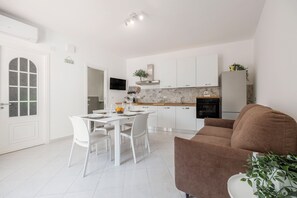 Une cuisine moderne avec des meubles blancs, une table à manger avec des chaises, un canapé et un téléviseur fixé au mur.