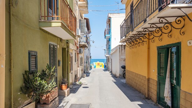 A narrow street with buildings on either side, a clear sky, and a distant view of the sea. - Holiday Home 'Piazzetta Al Mare' with Sea View, Wi-Fi and Air Conditioning (Palermo)