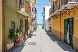 A narrow street with buildings on either side, a clear sky, and a distant view of the sea.
