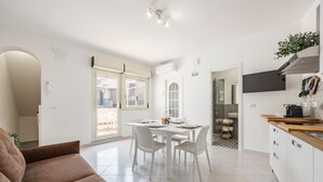 A modern kitchen with white cabinetry, a dining area with a white table and chairs, and a brown sofa in the living area. - Holiday Home 'Piazzetta Al Mare' with Sea View, Wi-Fi and Air Conditioning (Palermo)