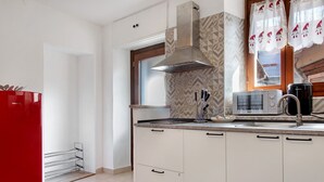 Une cuisine avec des armoires blanches, une hotte de cuisinière en acier inoxydable, un four à micro-ondes et un réfrigérateur rouge.