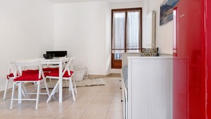 Une pièce comprenant une table à manger, des chaises, un réfrigérateur rouge, un meuble blanc et une fenêtre avec des rideaux.