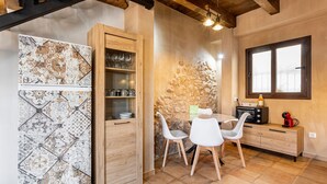 A kitchen with a stone wall, wooden cabinets, white chairs, and a window. - Estudio 'Vencejos' con Wi-Fi en Ademuz (Ademuz)