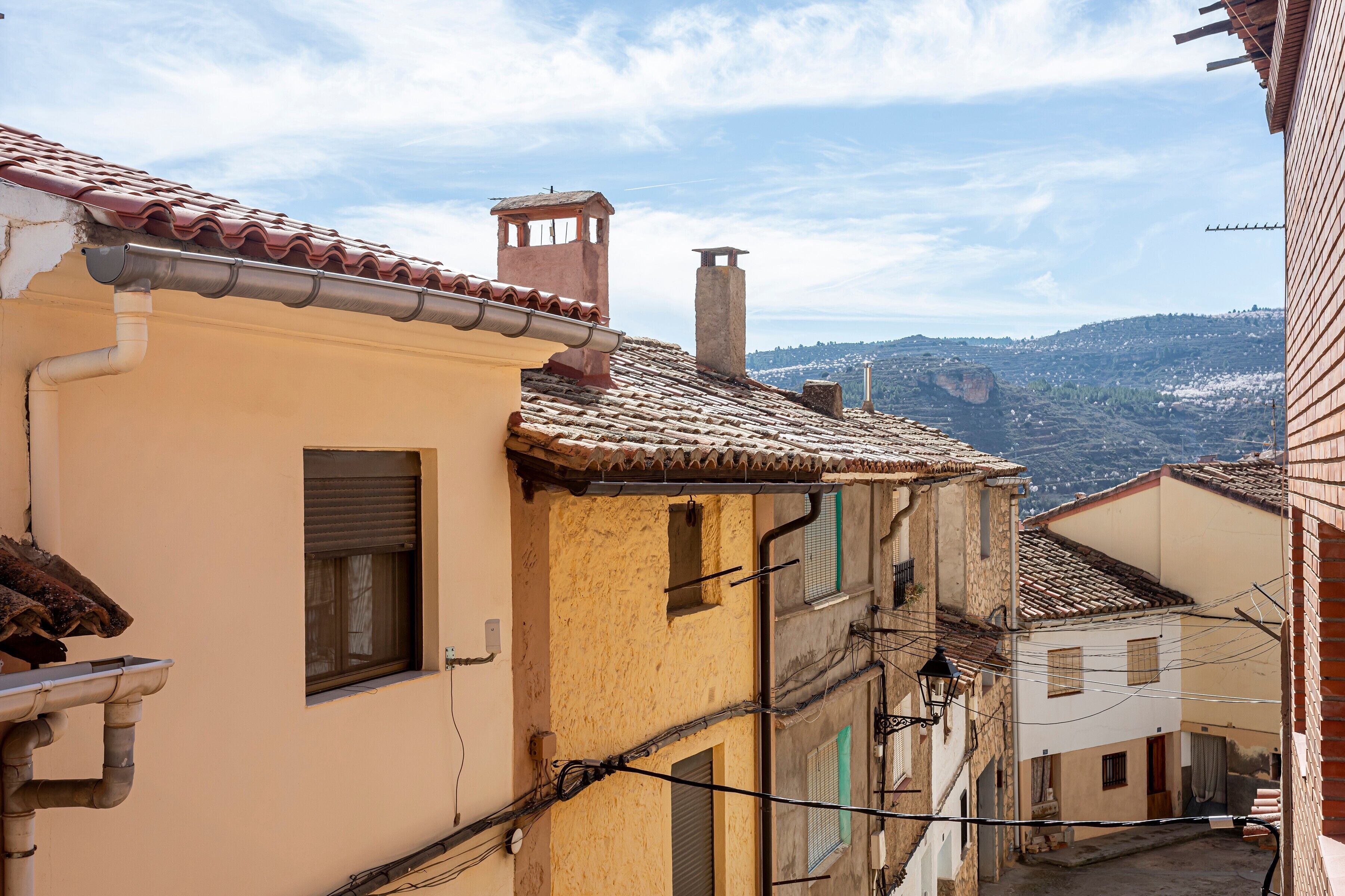 Una calle estrecha con edificios de techos de teja y vistas de un paisaje montañoso al fondo.