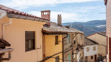 Una calle estrecha con edificios de techos de teja y vistas de un paisaje montañoso al fondo.
