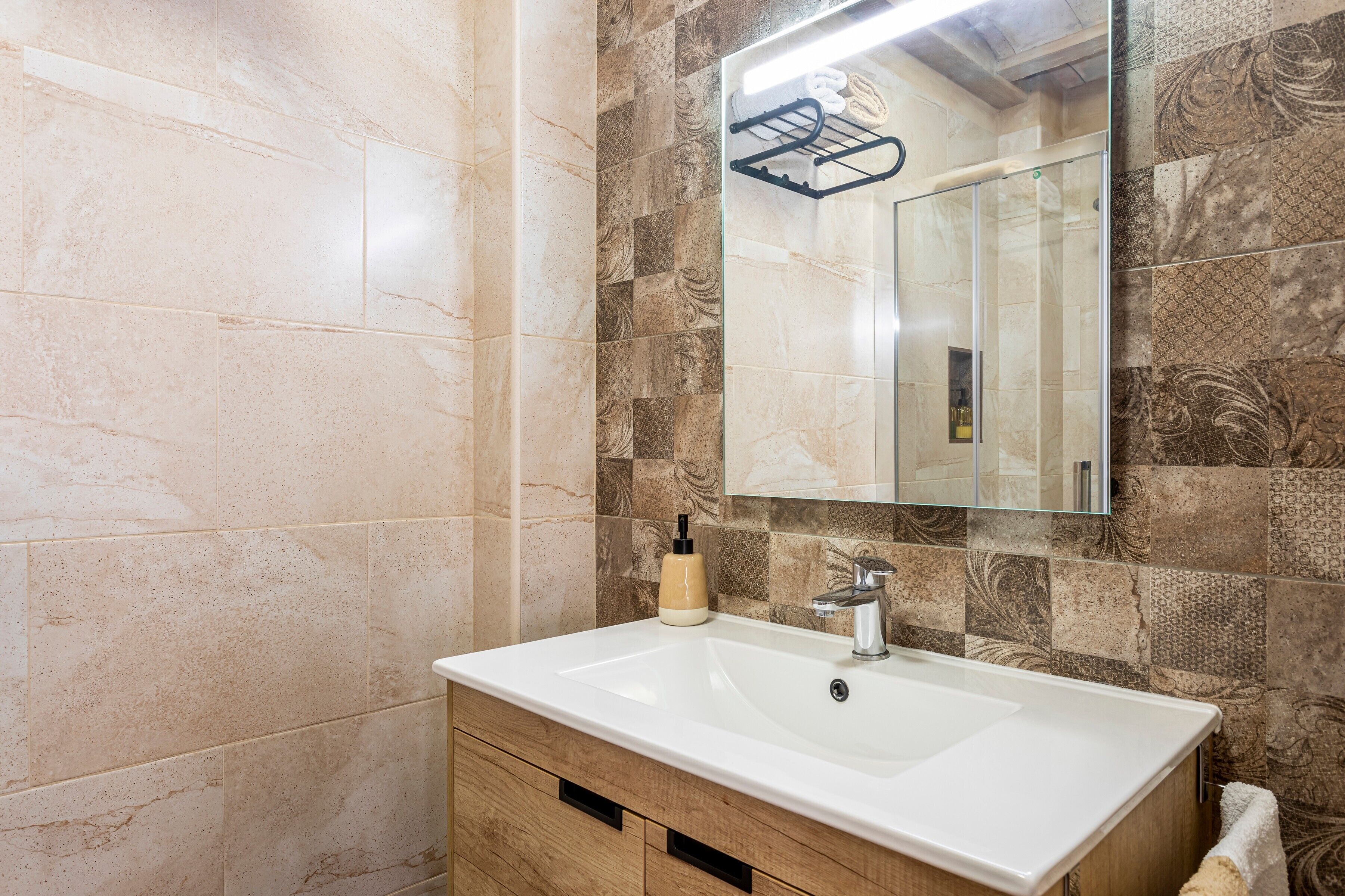 A bathroom with a white sink, a mirror, and patterned tiles.