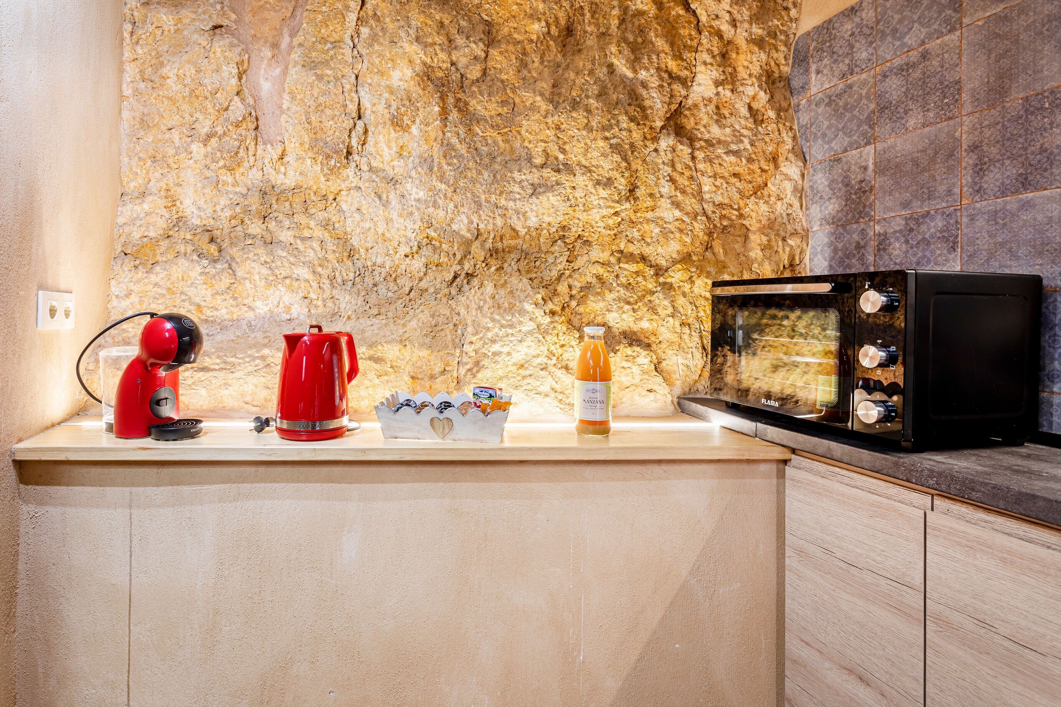 A kitchen with a stone wall, a red coffee maker, a microwave, and a wine bottle.