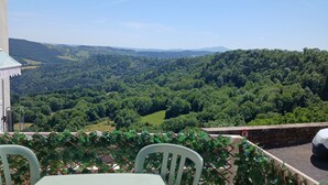 Una mesa y sillas en un balcón con vistas a un valle boscoso.