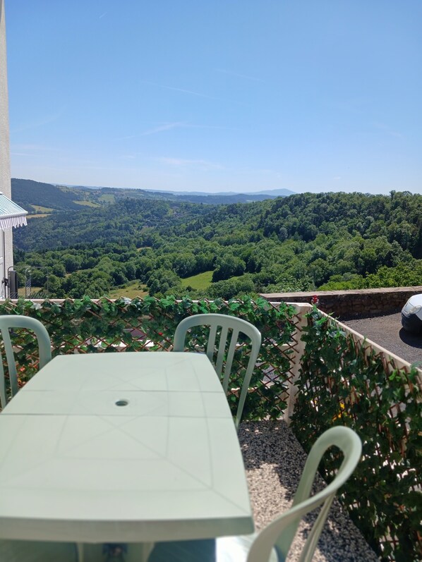 A table and chairs on a balcony with a view of a forested valley.