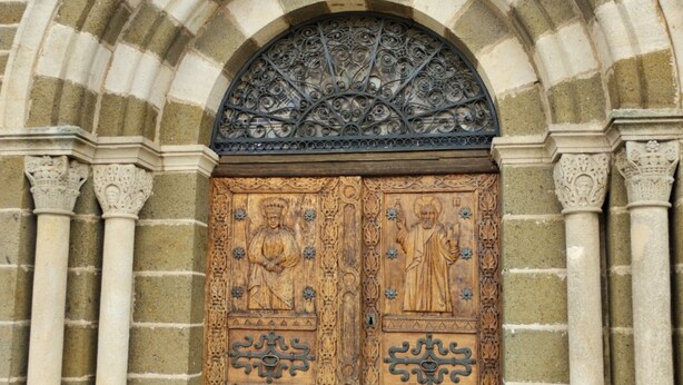 Una puerta doble de madera con intrincados grabados y un arco de metal encima.