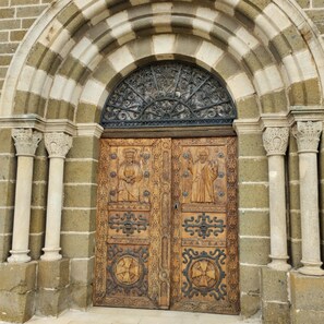 A wooden double door with intricate carvings and a metal arch above it.