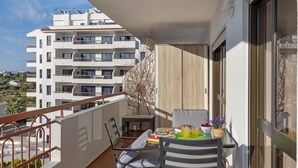 A balcony with a table, chairs, and a view of a multi-story building.