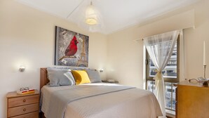 A bedroom with a bed, a nightstand, a dresser, a window with sheer curtains, and a wall painting.