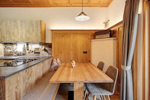 A wooden kitchen with a built-in island, a dining area with chairs, and a hanging light fixture.