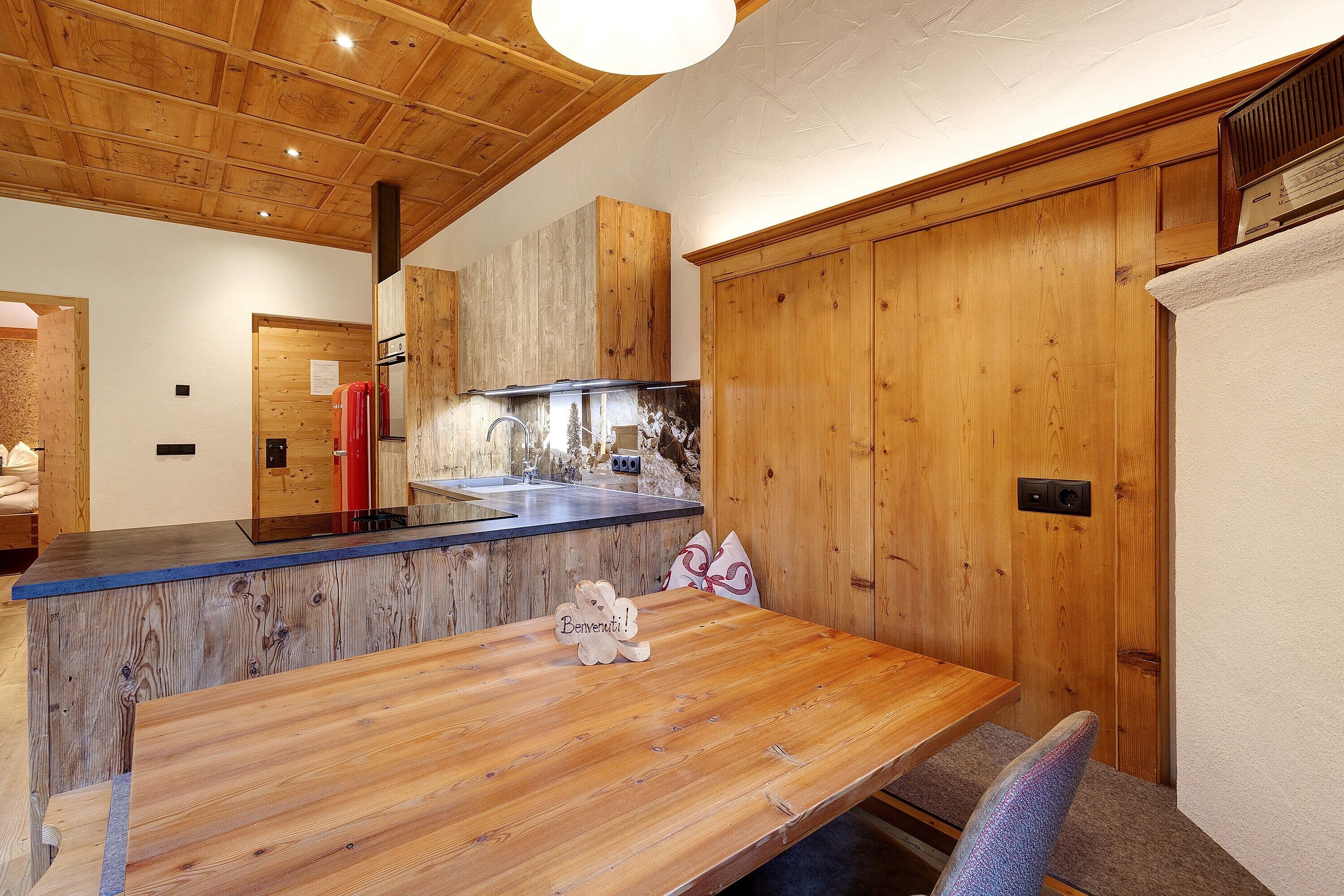 A wooden interior with a kitchen area, a dining table with a teddy bear, and a wooden door.