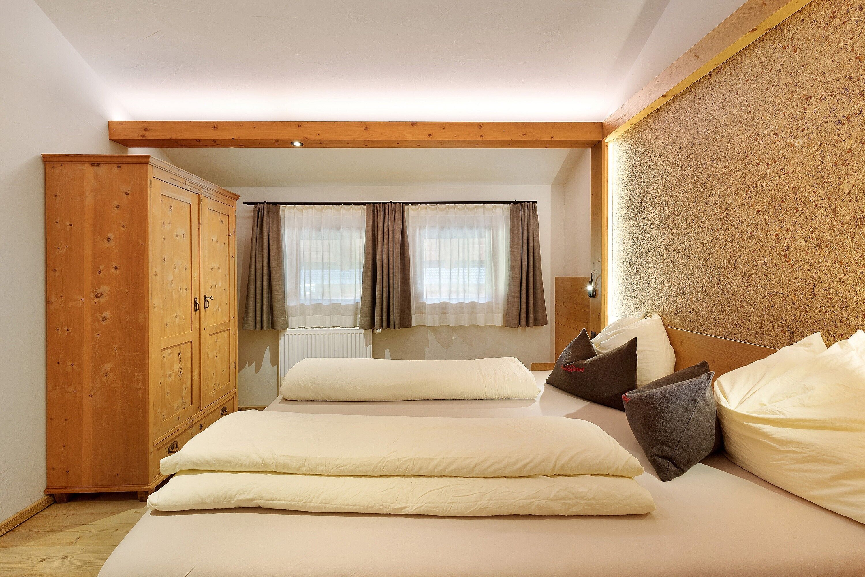 Une chambre avec une armoire en bois, un lit avec une literie blanche et une vue par la fenêtre, qui est ornée de rideaux.
