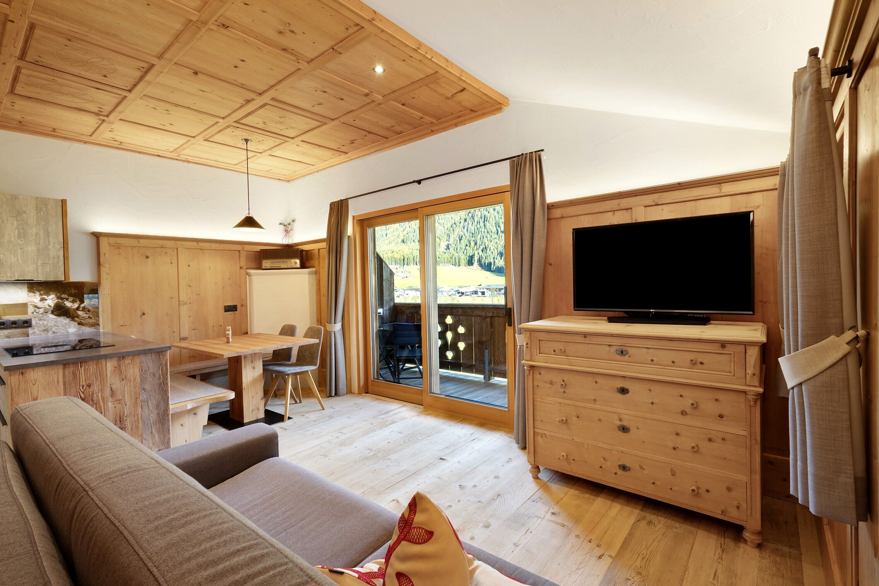 Un intérieur moderne avec un plafond en bois, un coin repas, un canapé, un téléviseur et une porte-fenêtre coulissante donnant sur un espace extérieur.