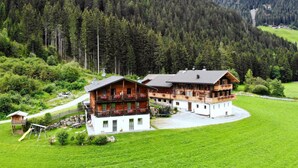Un chalet à deux étages doté d’un balcon, entouré d’un paysage verdoyant et luxuriant et de montagnes boisées.