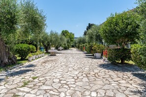 A stone-paved pathway flanked by trees and potted plants, leading to a distant building. - Studio 'Alexandros Studios 5' with Shared Pool, Wi-Fi and Air Conditioning (Roda)