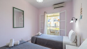 A room with two beds, a window with a view of buildings, a mirror, and a wall-mounted lamp. - Studio 'Alexandros Studios 5' with Shared Pool, Wi-Fi and Air Conditioning (Roda)