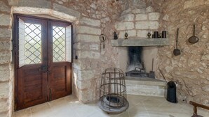 A stone-walled room with a fireplace, a wooden door with glass panels, and a metal rack.