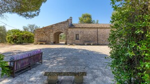 A stone building with an arched entrance, a tiled roof, and a bench in the foreground.