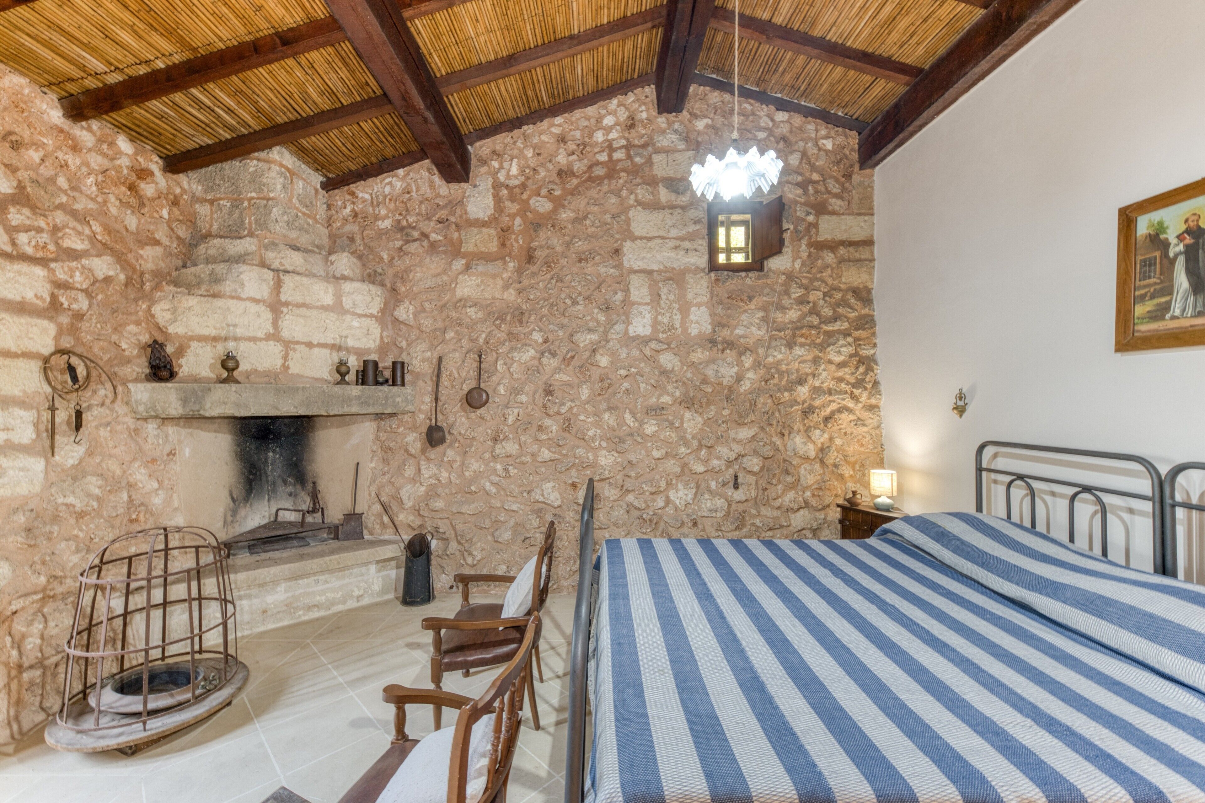 A stone-walled room with a bed, a fireplace, and a hanging light fixture.
