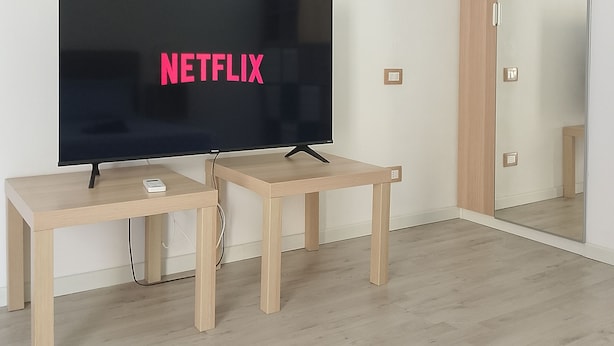 A modern room with a large flat-screen TV on a wooden stand, a small table, and a mirror on the wall. - Messina Apartments (Messina)