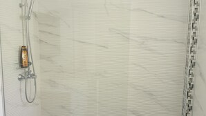 A walk-in shower with a glass door, a handheld showerhead, and a wall-mounted faucet. - Messina Apartments (Messina)