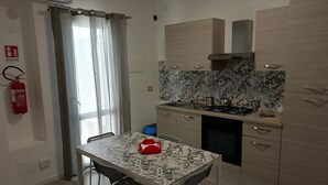 A compact kitchen with a dining area, featuring a patterned tile backsplash, wooden cabinets, and a gas stove. - Messina Apartments (Messina)