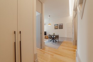 Um corredor que dá para uma sala de jantar, com uma mesa e cadeiras, um lustre pendurado e uma porta.