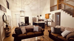 A spacious living area with a high ceiling, a staircase, and a kitchen in the background. - Lake House With Beach Access, Theater, Hot Tub (Port Austin)