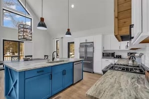 Una cocina moderna con una isla grande, armarios blancos y un refrigerador de acero inoxidable.