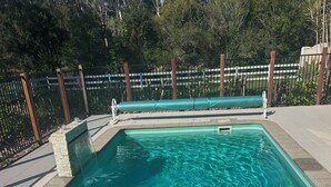 Une piscine rectangulaire à l’eau claire, entourée d’une clôture et d’arbres.