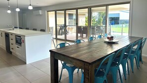 Une cuisine moderne dotée d’un îlot central, d’un coin repas avec des chaises bleues et de grandes portes-fenêtres coulissantes donnant sur une terrasse.