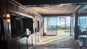 Um corredor espaçoso com cozinha à esquerda, uma grande porta de correr de vidro que dá para uma piscina e área de estar ao ar livre, e vista para o oceano.