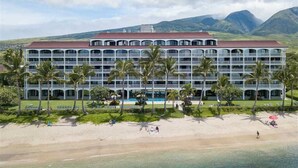 Um hotel grande com várias varandas e área de piscina, cercado por palmeiras e montanhas ao fundo.