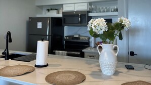Une cuisine moderne avec un plan de travail blanc, un robinet noir, un porte-serviettes en papier, un vase blanc avec des fleurs et un évier en acier inoxydable.