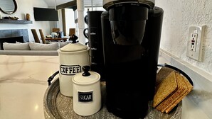 Un comptoir de cuisine avec une machine à café, un récipient à sucre et un plateau avec du pain.