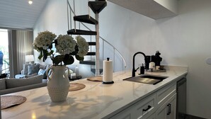 Une cuisine moderne dotée d’un plan de travail en marbre, d’un évier encastré et d’un escalier menant à un niveau supérieur.