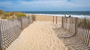 A sandy beach path leading to the ocean, bordered by wooden fences.