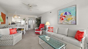 A modern living room with a dining area, a kitchen in the background, and a ceiling fan.