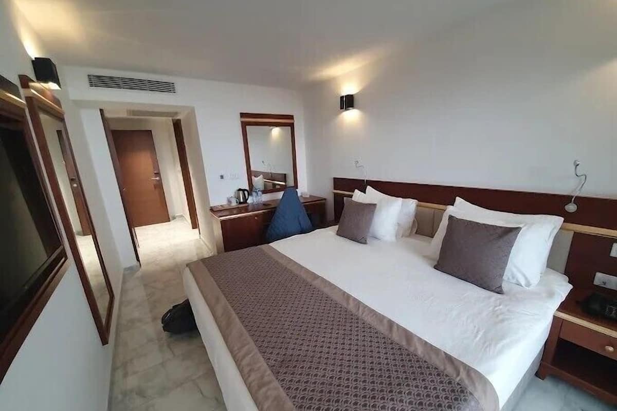 Una camera d'albergo con un letto grande, comodini, uno specchio e una porta che dà su un'altra stanza.