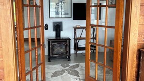 Eine Holztür mit Glasschilden führt in einen Raum mit Kamin, einem gerahmten Bild an der Wand und einem kleinen Tisch.