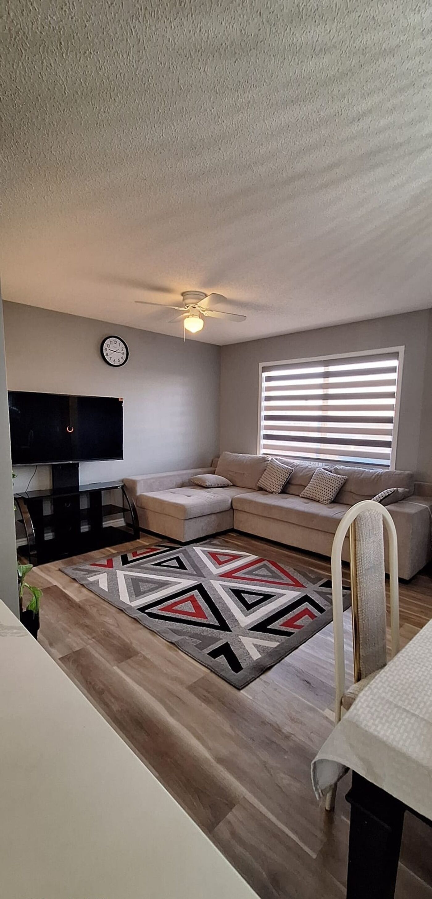 A living room with a sofa, a television, a ceiling fan, and a window with blinds.