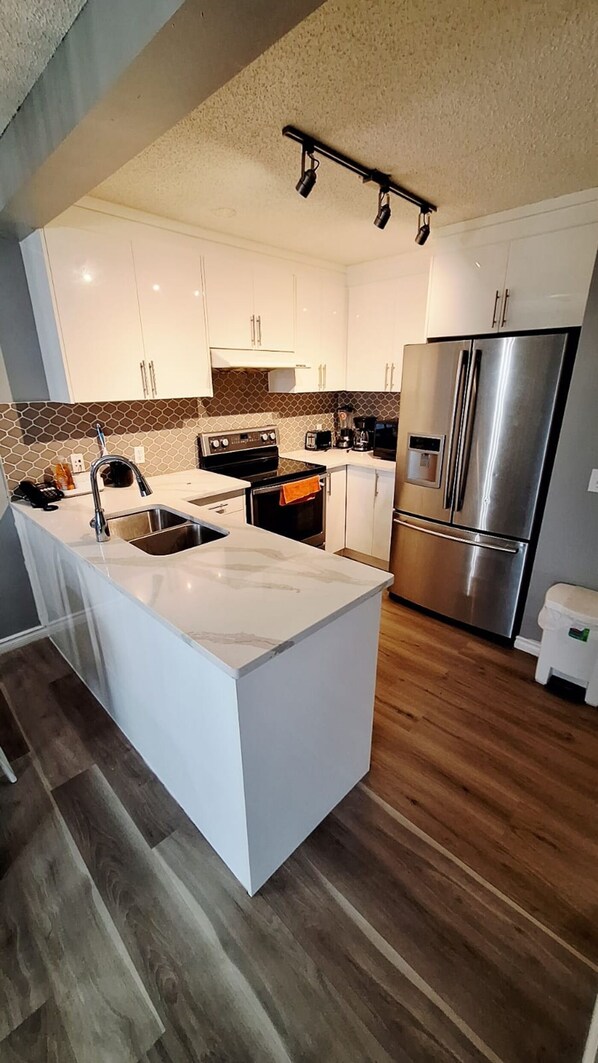 Una cocina moderna con armarios blancos, una isla grande con un fregadero, un refrigerador de acero inoxidable y un microondas.