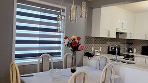 Ein Essbereich mit einem Tisch für vier Personen, einer Vase mit Blumen und einer Küche im Hintergrund.