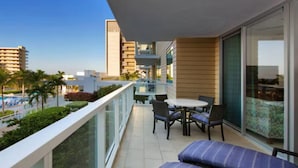Un balcón con una mesa y sillas, un sofá y vistas a una piscina y edificios.