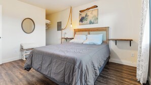 Quarto com cama, cabeceira de madeira, mesa de cabeceira com abajur, espelho fixado na parede e arte com mapa.